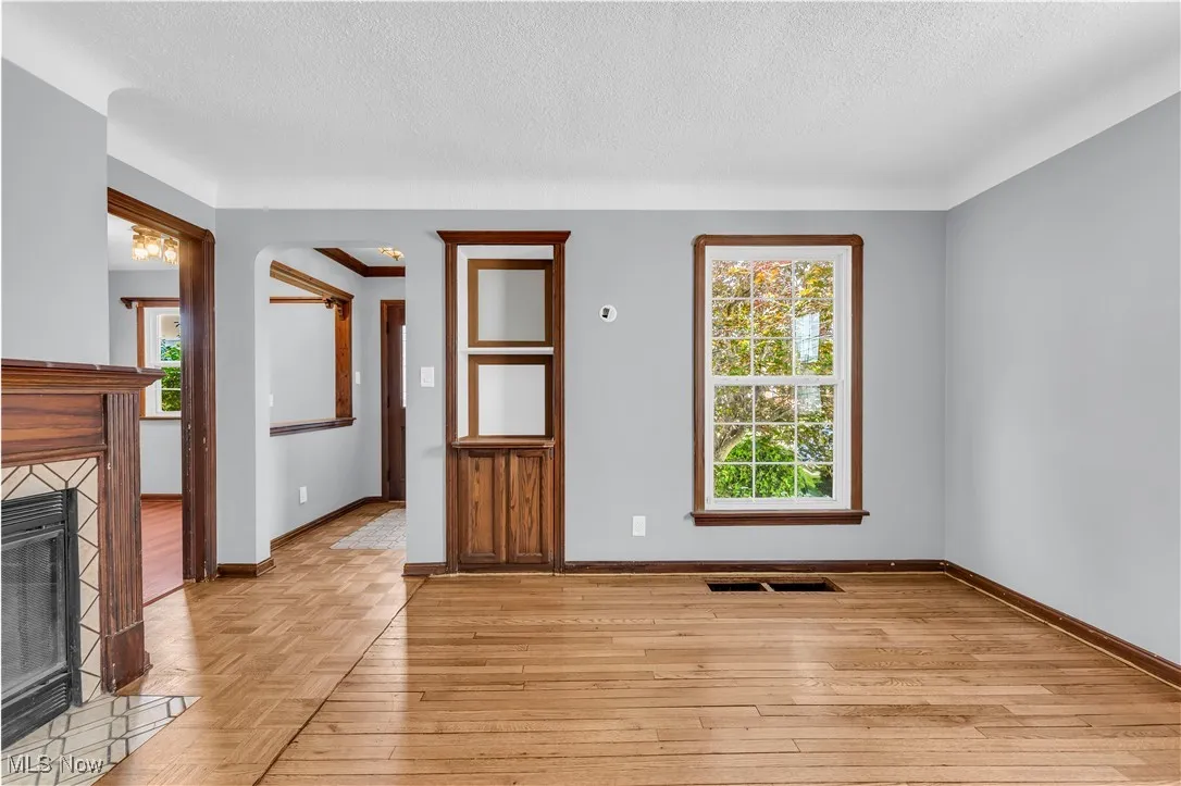 Unfurnished living room with a textured ceiling, baseboards, a fireplace, light wood-style floors, and arched walkways