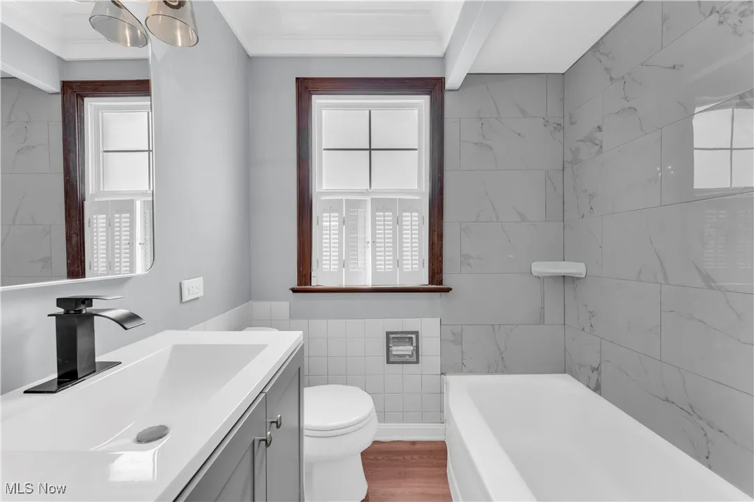 Bathroom featuring a bath, toilet, vanity, tile walls, and wood finished floors
