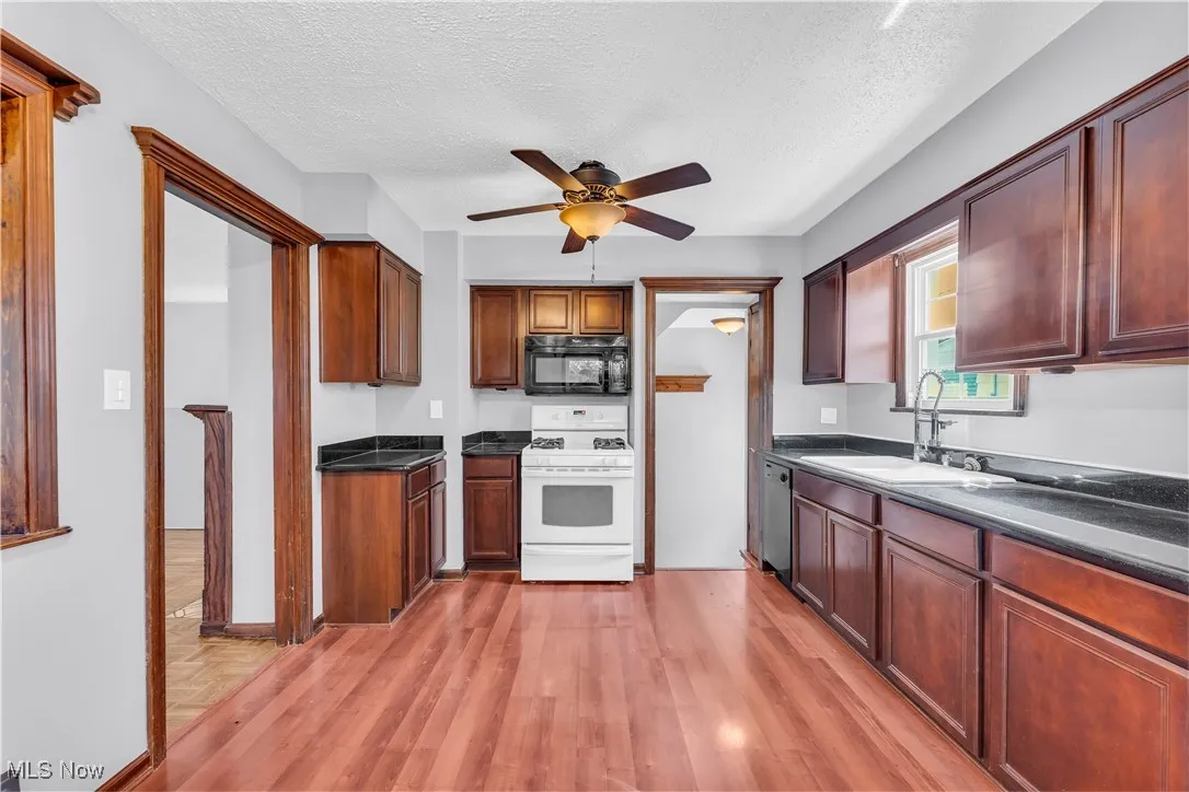 Kitchen featuring white gas stove, black microwave, a sink, a ceiling fan, and light wood-type flooring