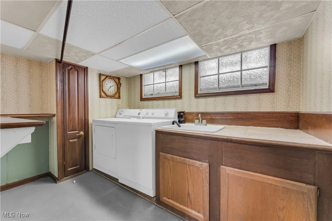 Laundry area featuring a sink, washer and dryer, and wallpapered walls