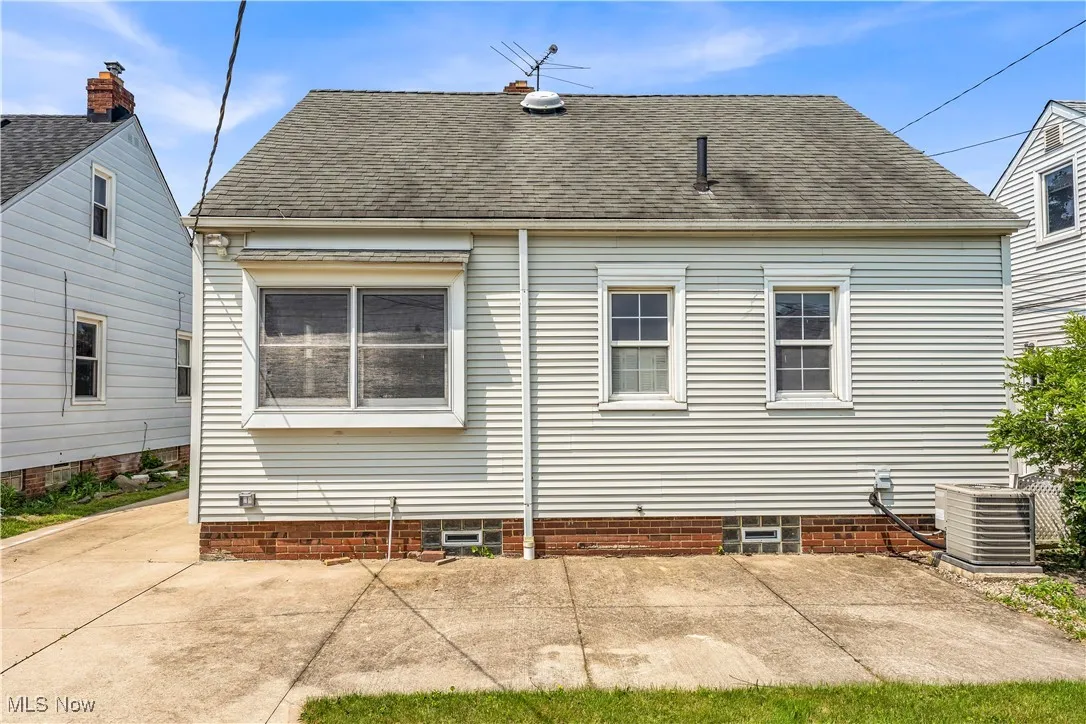 Rear view of property featuring central AC unit, roof with shingles, and a patio area