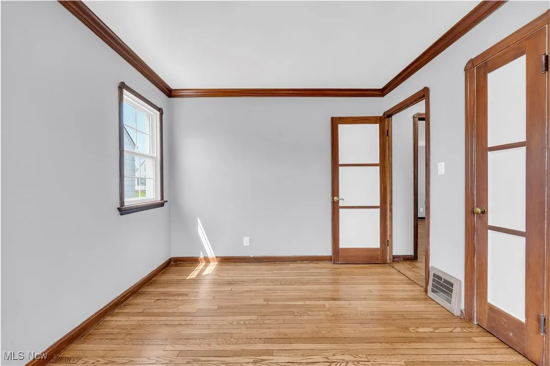 Empty room featuring crown molding, light wood-type flooring, and baseboards