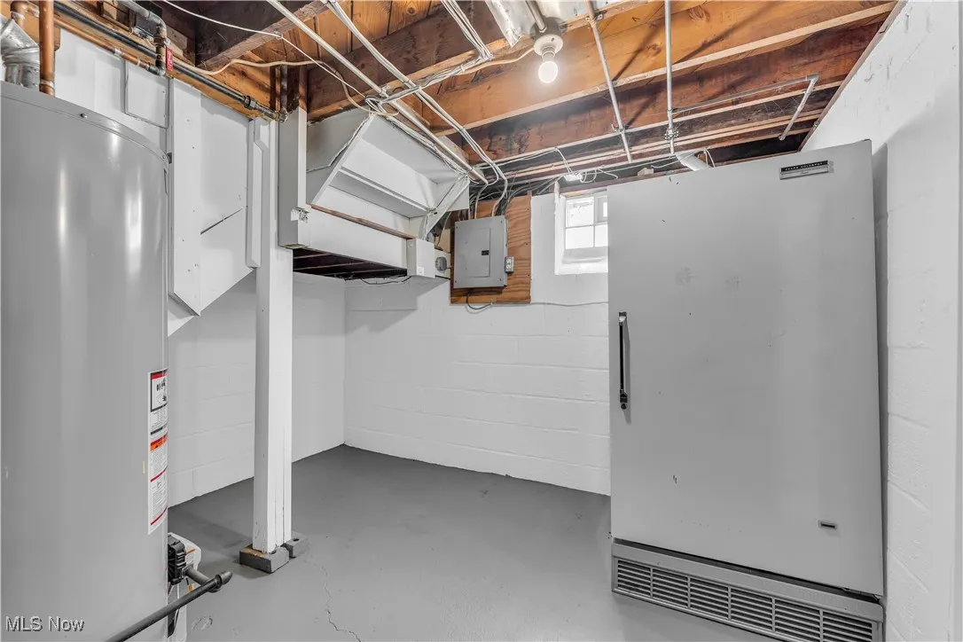 Below grade area featuring gas water heater, electric panel, and freestanding refrigerator