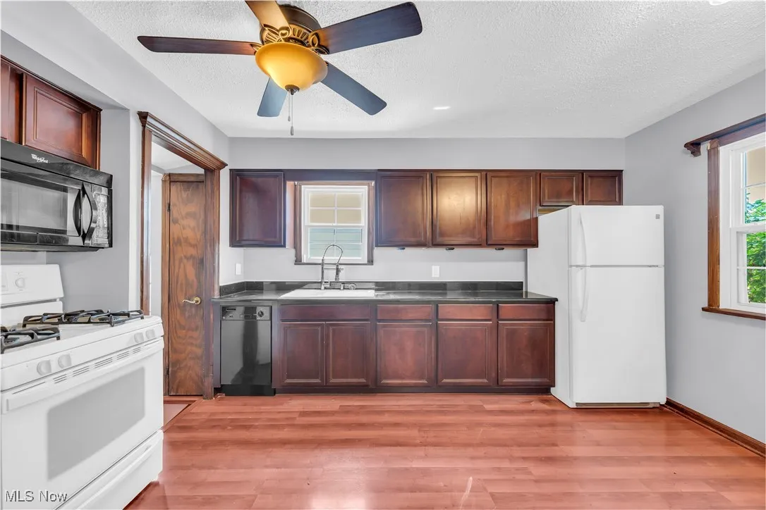 Kitchen featuring white appliances, a sink, light wood-style floors, a textured ceiling, and ceiling fan