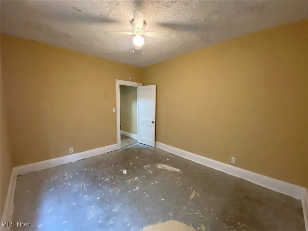 Empty room featuring baseboards, ceiling fan, and a textured ceiling