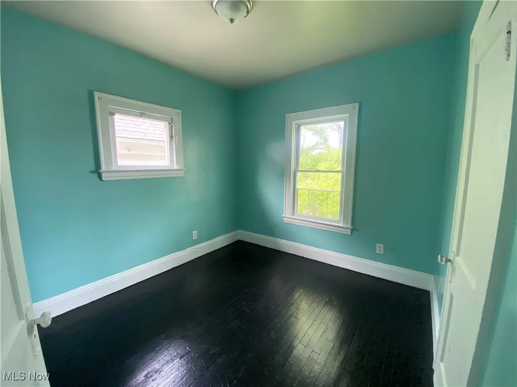 Empty room featuring healthy amount of natural light, dark wood-type flooring, and baseboards
