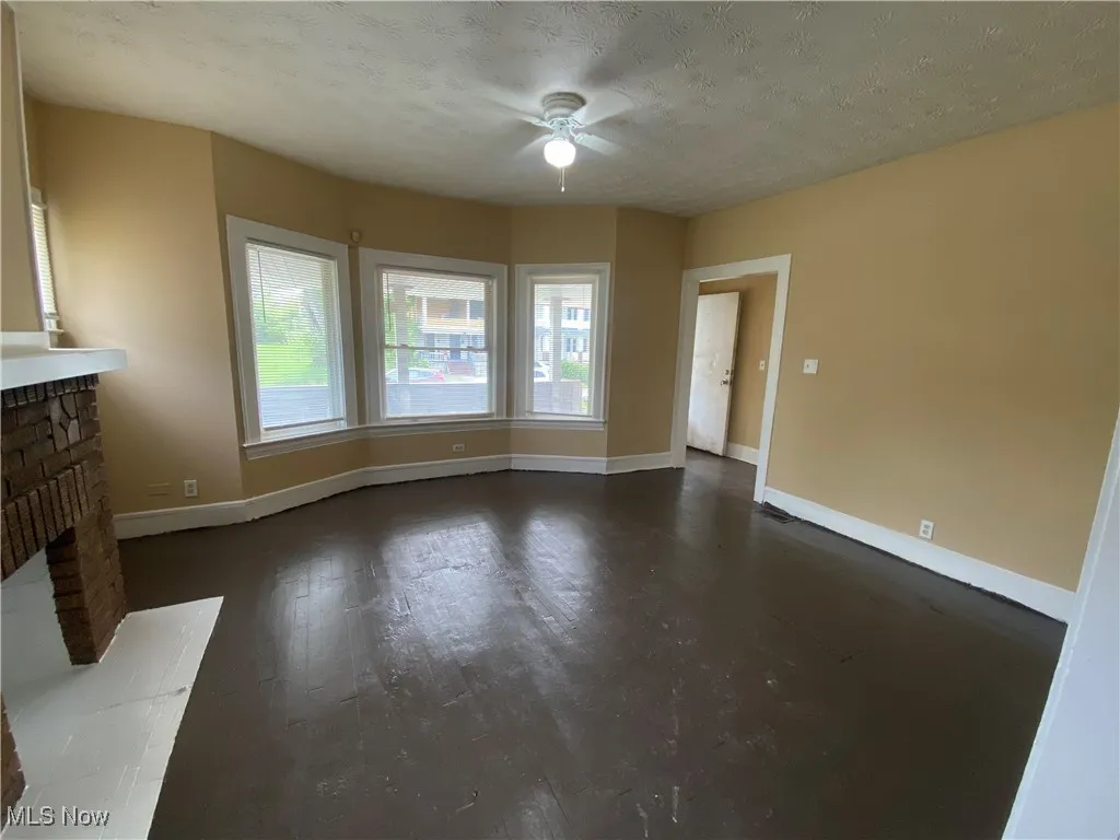 Unfurnished living room featuring ceiling fan, baseboards, a fireplace, dark wood finished floors, and a textured ceiling