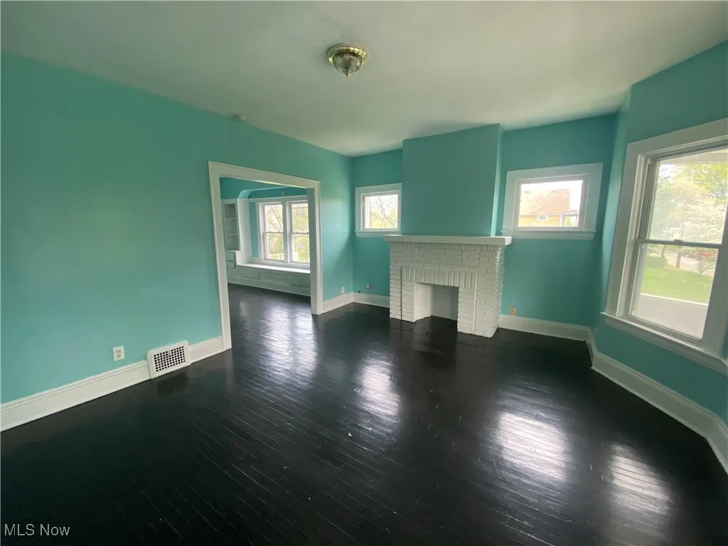 Unfurnished living room with a brick fireplace, wood finished floors, and baseboards