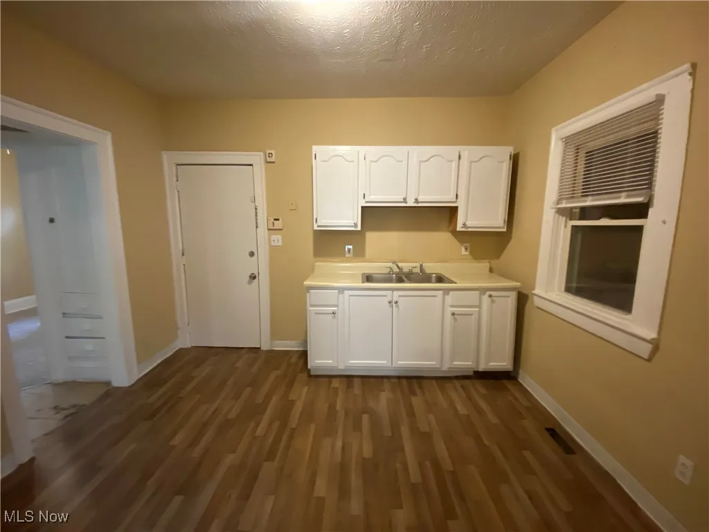 Kitchen with a sink, white cabinetry, dark wood-type flooring, baseboards, and a textured ceiling