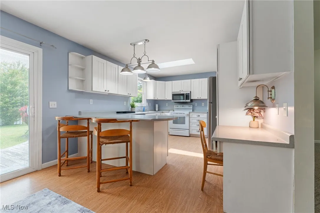 Kitchen with stainless steel appliances, light wood finished floors, a breakfast bar, and white cabinetry