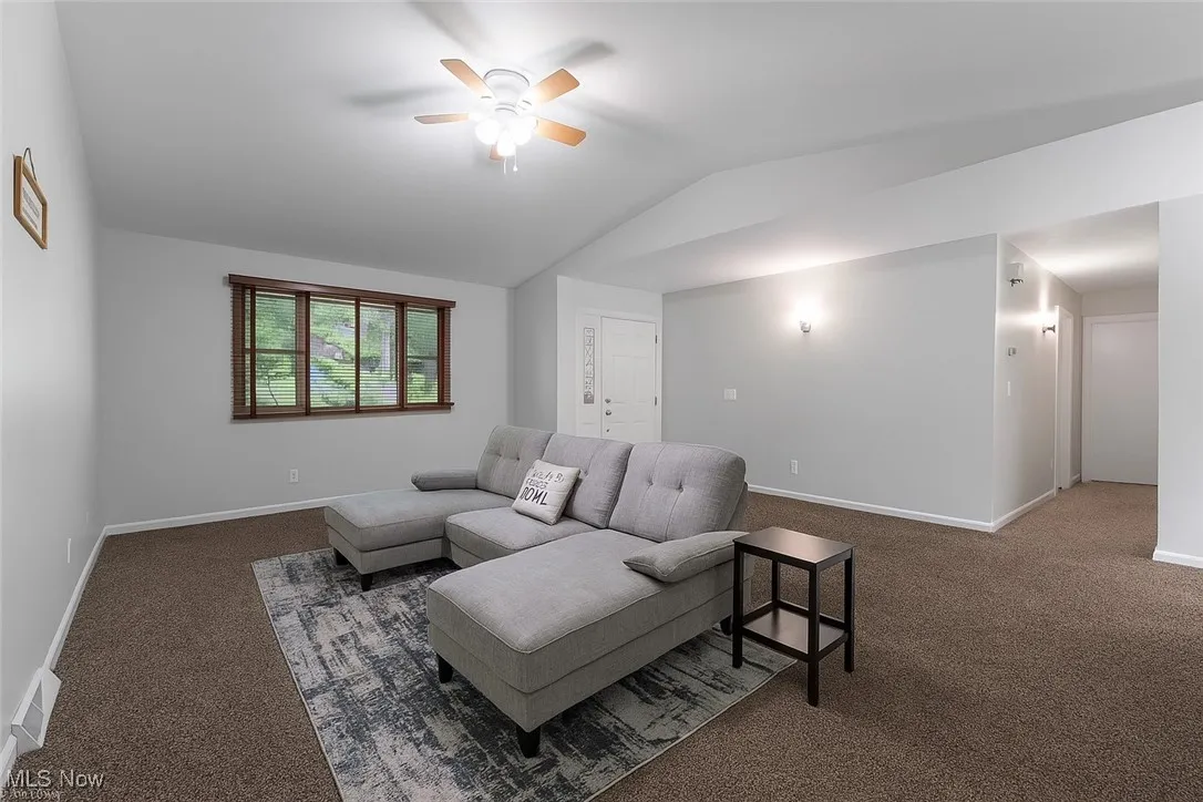 Carpeted living area featuring vaulted ceiling and ceiling fan