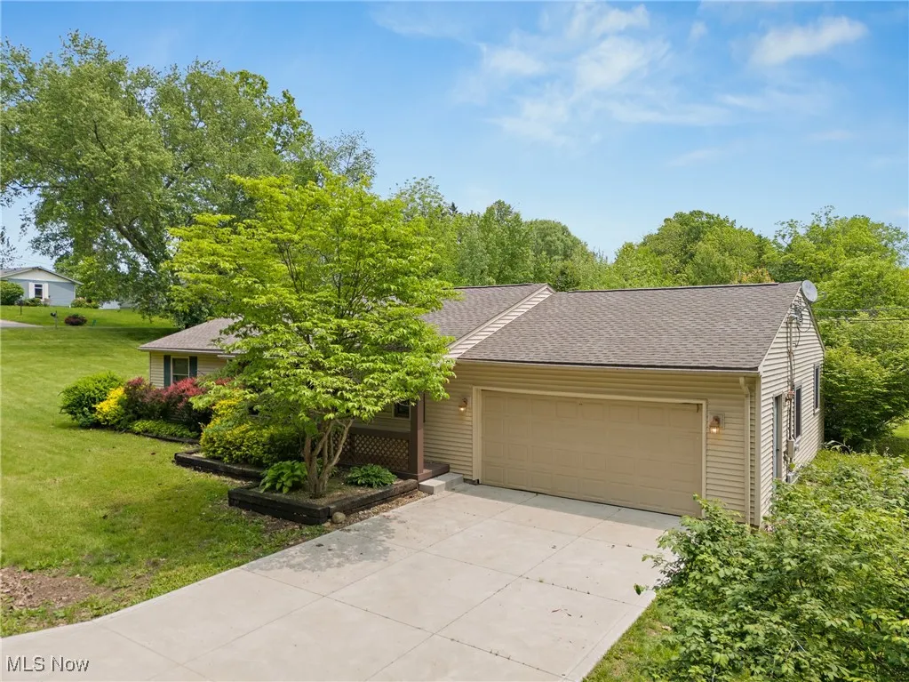 View of property hidden behind natural elements featuring an attached garage, concrete driveway, and a front lawn