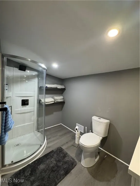 Full bath featuring a stall shower, toilet, wood finished floors, and baseboards