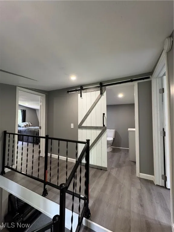 Staircase with a barn door, wood finished floors, and baseboards