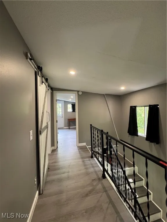 Corridor with a barn door, wood finished floors, plenty of natural light, baseboards, and recessed lighting