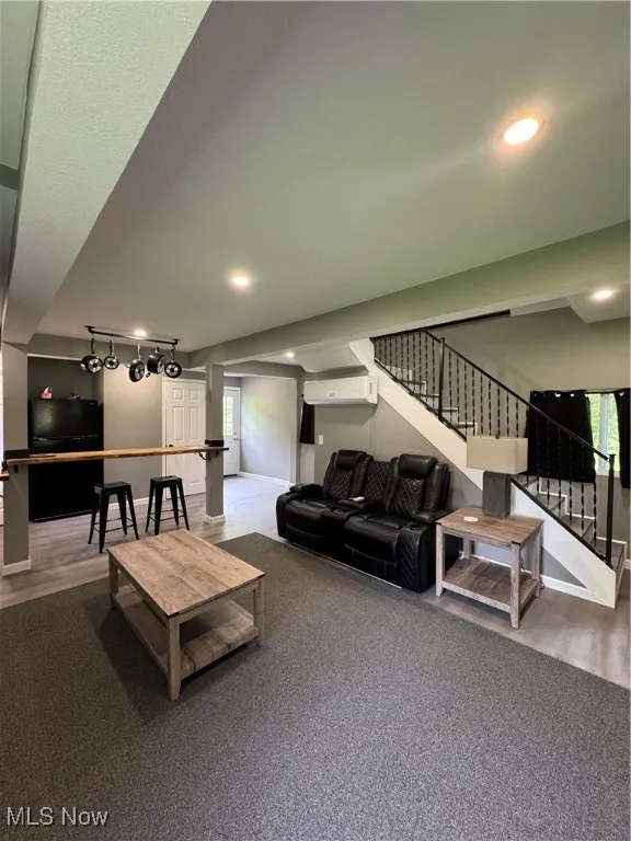 Living area featuring a wall mounted air conditioner, stairway, healthy amount of natural light, wood finished floors, and recessed lighting
