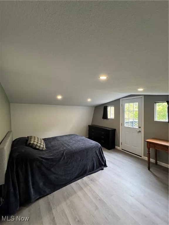 Bedroom featuring light wood finished floors, lofted ceiling, a textured ceiling, baseboards, and recessed lighting