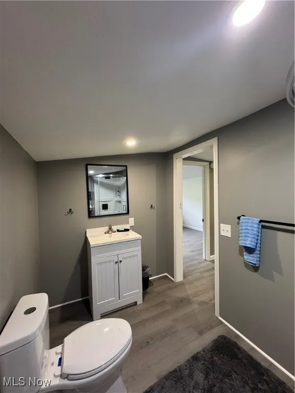 Half bath with toilet, vanity, wood finished floors, and baseboards