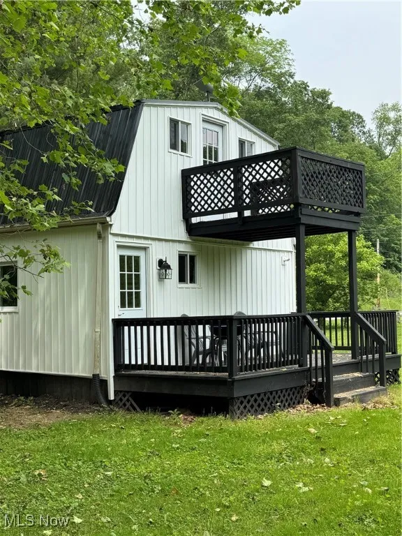 Rear view of house featuring a balcony, a lawn, and a wooden deck