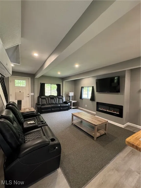 Living area featuring recessed lighting, a glass covered fireplace, healthy amount of natural light, baseboards, and wood finished floors