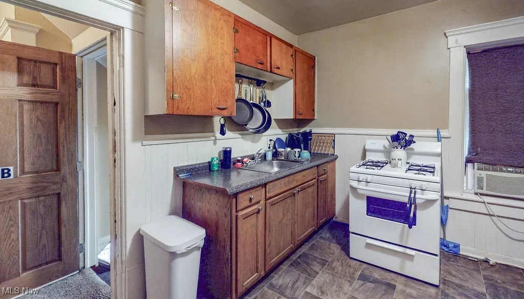 Kitchen with gas range gas stove, a sink, wainscoting, dark countertops, and brown cabinets