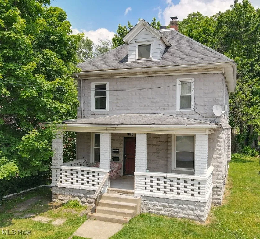 American foursquare style home featuring a porch, a chimney, stone siding, and a shingled roof