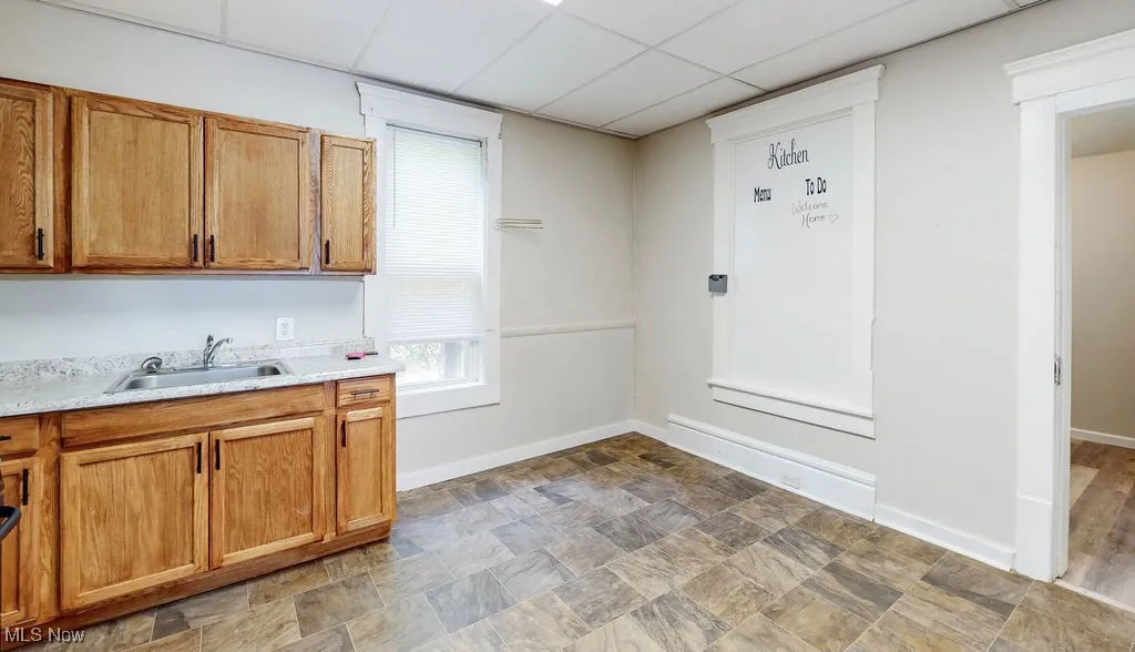 Kitchen featuring a sink, light countertops, brown cabinetry, baseboards, and a paneled ceiling
