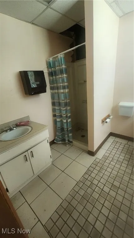 Full bathroom featuring a stall shower, a paneled ceiling, baseboards, vanity, and tile patterned floors