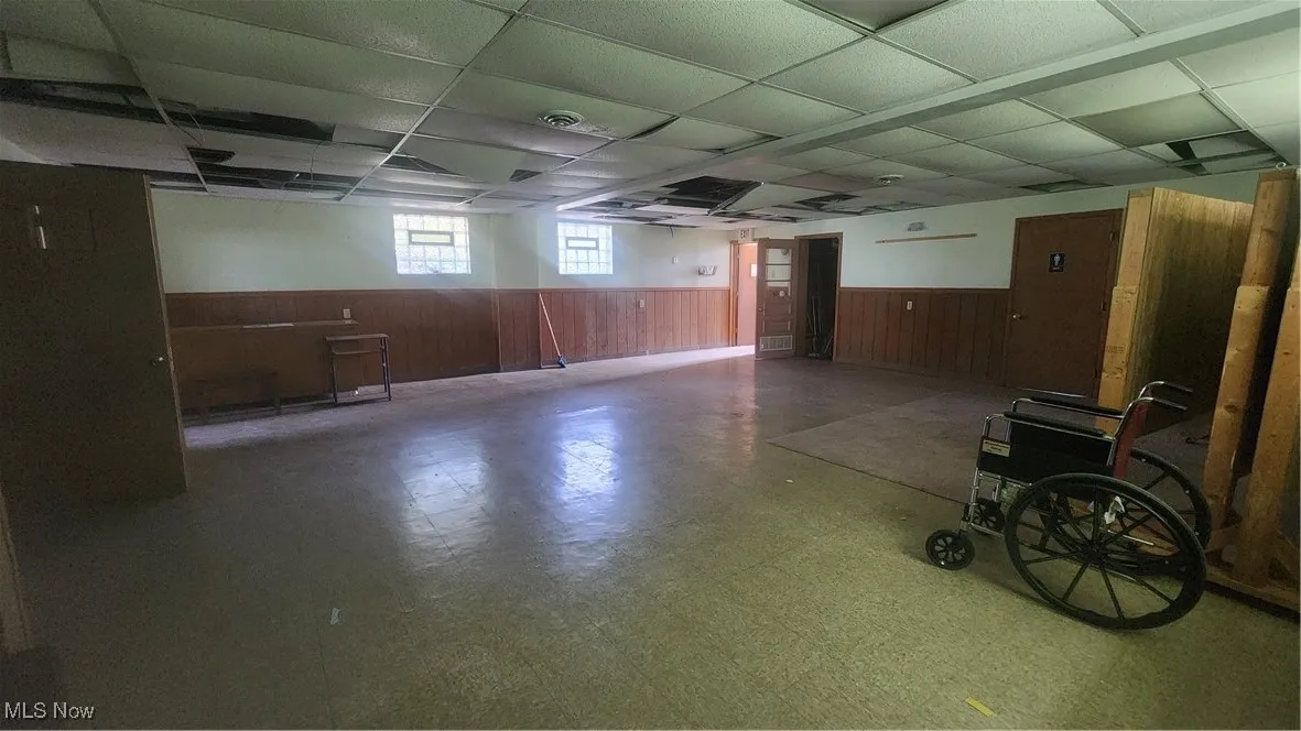 Basement with a wainscoted wall, a paneled ceiling, tile patterned floors, and wood walls