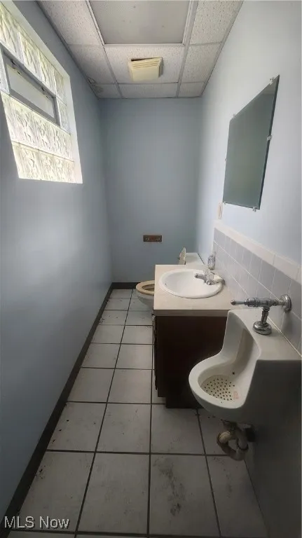 Bathroom featuring toilet, a paneled ceiling, tile patterned floors, vanity, and decorative backsplash