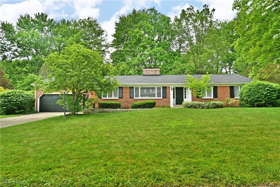 Single story home featuring brick siding, concrete driveway, a chimney, an attached garage, and a front yard