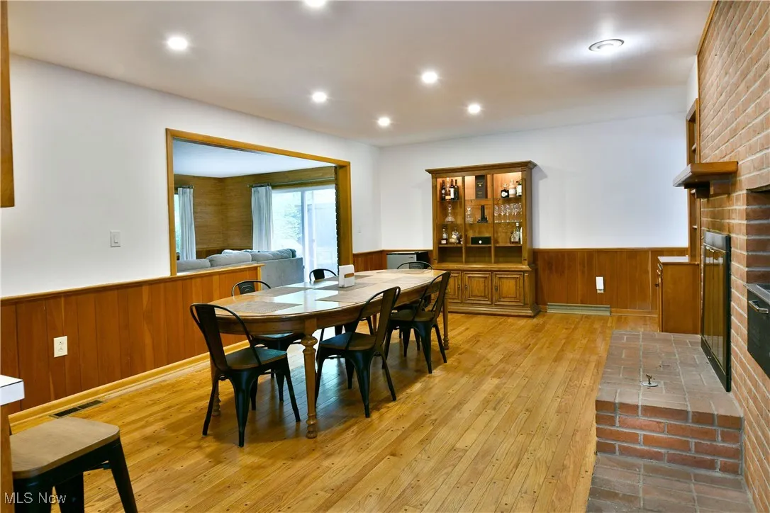 Dining room featuring a wainscoted wall, light wood-type flooring, wood walls, a fireplace, and recessed lighting