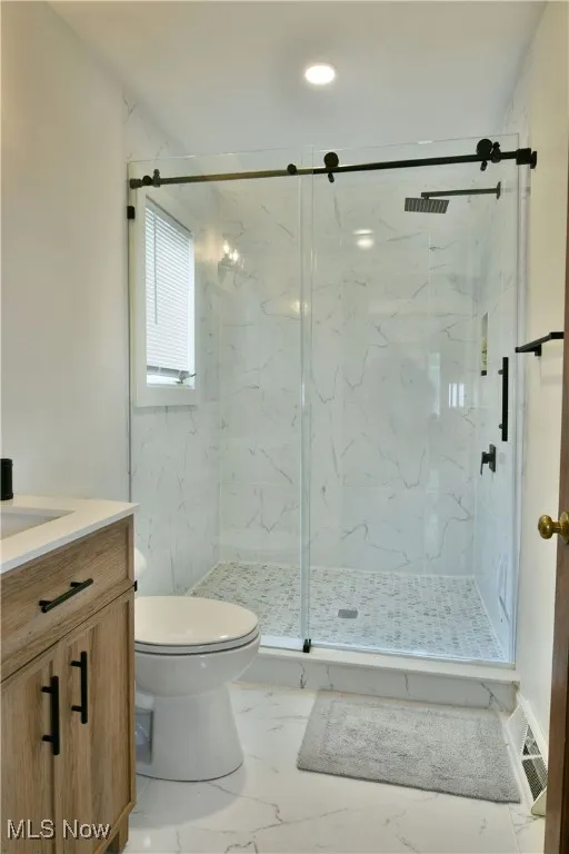 Bathroom with toilet, a marble finish shower, marble look tiles, and vanity