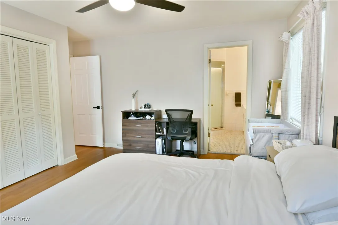 Bedroom with wood finished floors, connected bathroom, a ceiling fan, and a closet