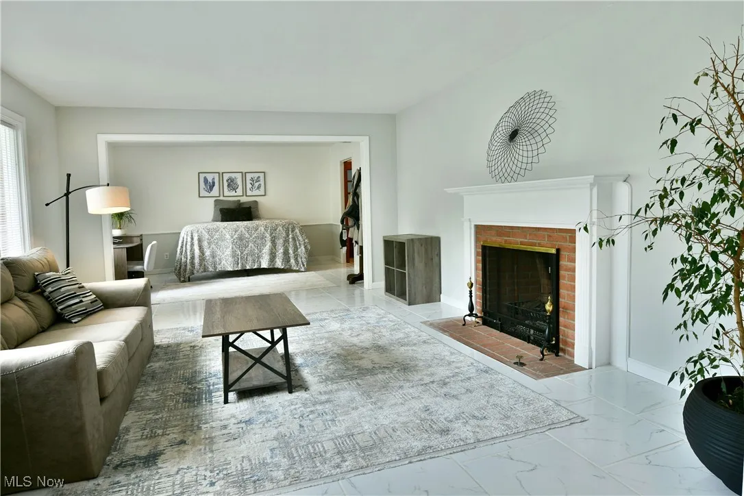 Living area with marble look tile flooring, a brick fireplace, and baseboards