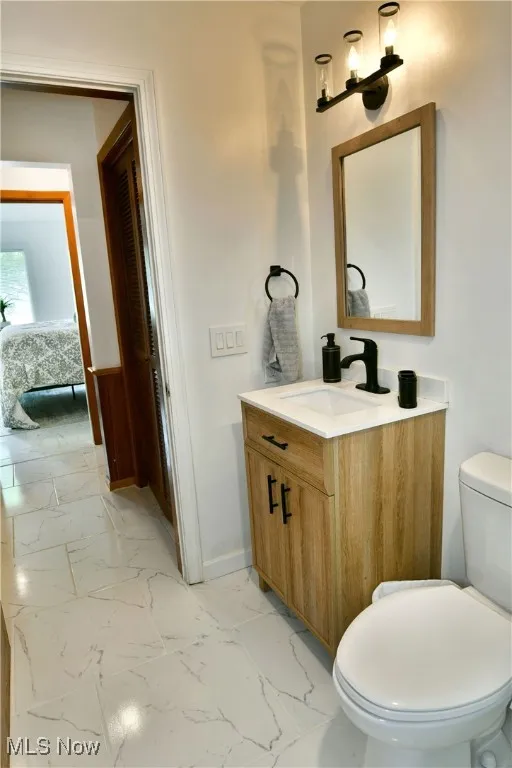 Ensuite bathroom featuring vanity, baseboards, marble look tiles, and toilet