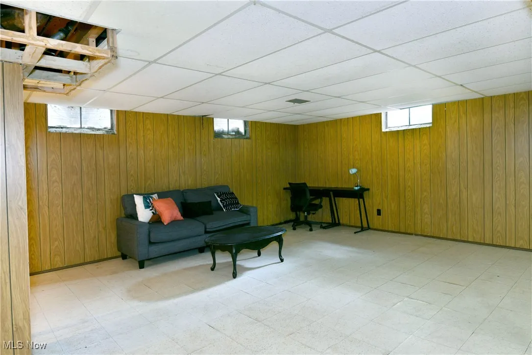 Living room featuring light flooring, a drop ceiling, wood walls, and plenty of natural light