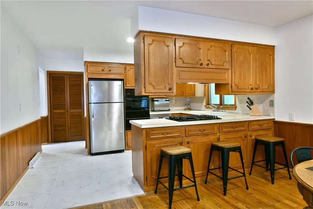 Kitchen with black appliances, a wainscoted wall, wooden walls, a peninsula, and brown cabinetry