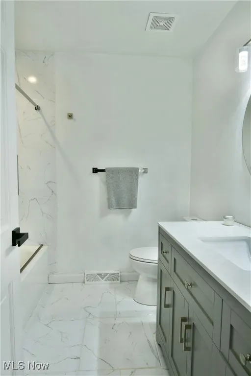 Bathroom with vanity, toilet, marble look tiles, and a combined bath / shower with marble appearance