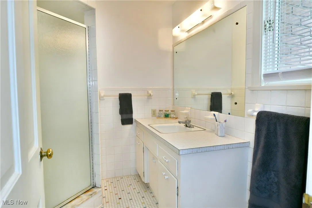 Full bathroom with vanity, tile walls, a stall shower, tile patterned flooring, and wainscoting