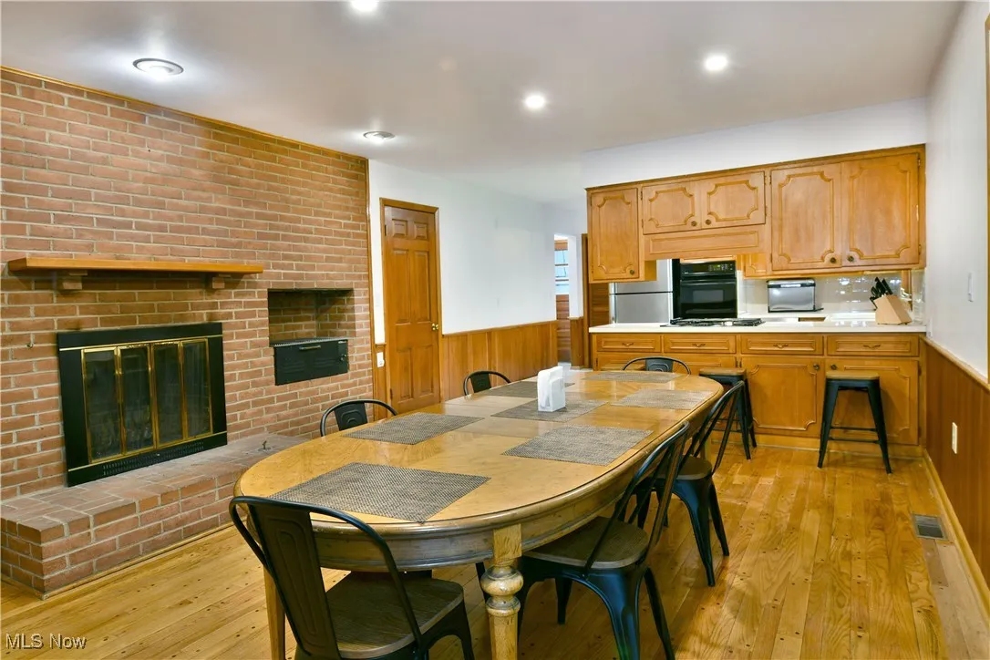 Dining area featuring wainscoting, light wood-type flooring, a fireplace, wood walls, and recessed lighting