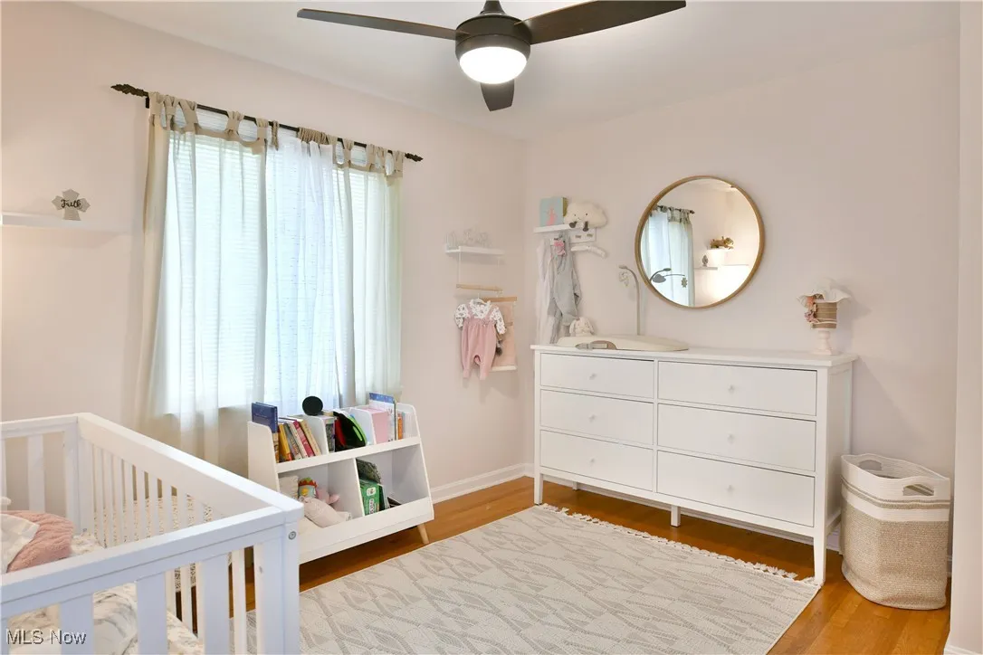 Bedroom featuring multiple windows, a crib, wood finished floors, and ceiling fan