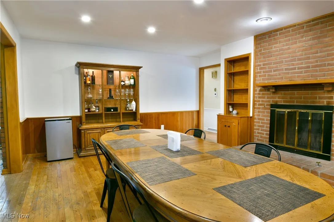 Dining area with wainscoting, wood walls, a brick fireplace, light wood-style floors, and recessed lighting