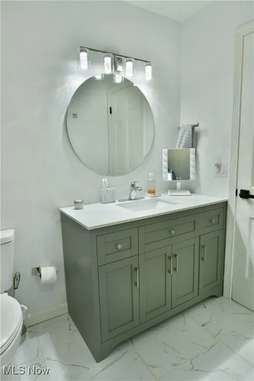 Bathroom with toilet, marble finish flooring, vanity, and baseboards