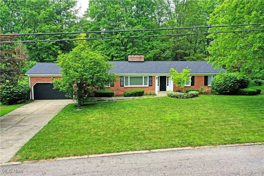 Ranch-style home with brick siding, driveway, a front lawn, and a chimney