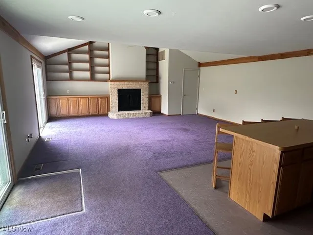 Unfurnished family room featuring carpet flooring, vaulted ceiling, and a fireplace