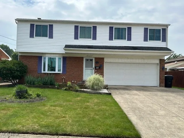 View of front of house featuring brick siding, an attached garage, a front yard, and driveway
