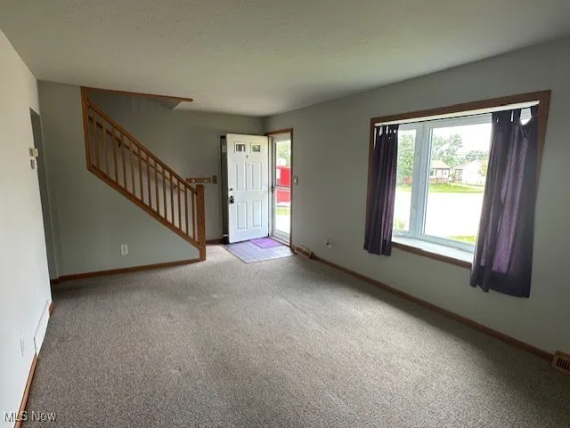 Foyer entrance with carpet flooring, stairway, and baseboards