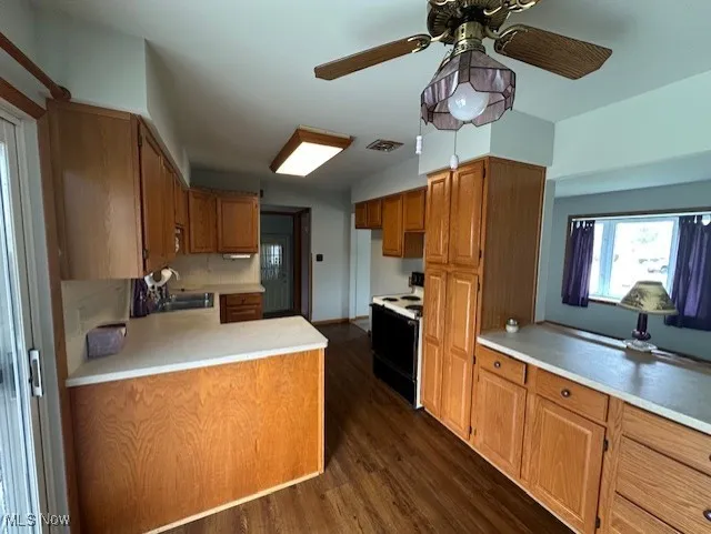 Kitchen with electric stove, a sink, light countertops, ceiling fan, and dark wood-type flooring