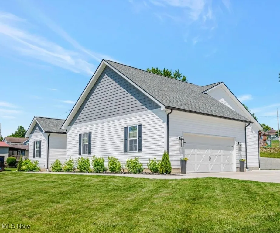 View of side of home featuring a yard, concrete driveway, a shingled roof, and an attached garage